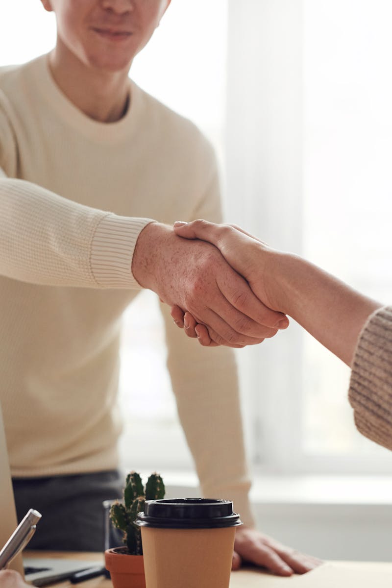 Close-up of professionals shaking hands over coffee in a modern office.